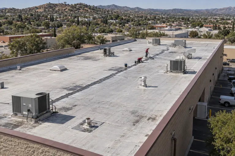 Two roofers patching a section of a flat warehouse roof between rooftop units in Nogales