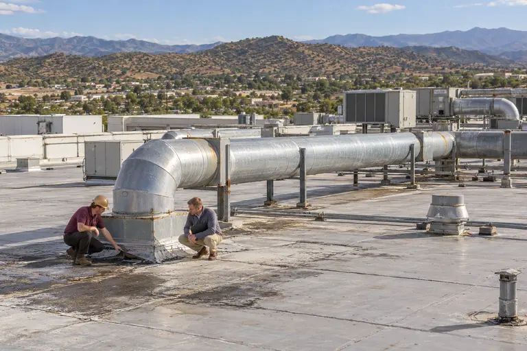 Roofer and plant manager kneeling beside rooftop ductwork on an industrial roof